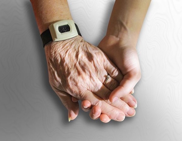 Aging parents 102: Image of younger hand holding older hand wearing an emergency alert bracelet.